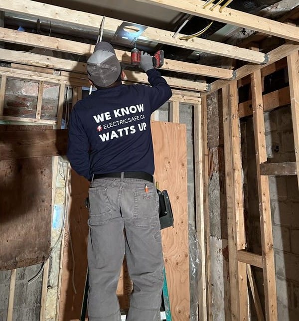 A skilled ElectricSafe technician works diligently on Hamilton home electrical inspections, wearing a shirt with the slogan "We Know Watts Up," demonstrating their expertise and commitment to safety.